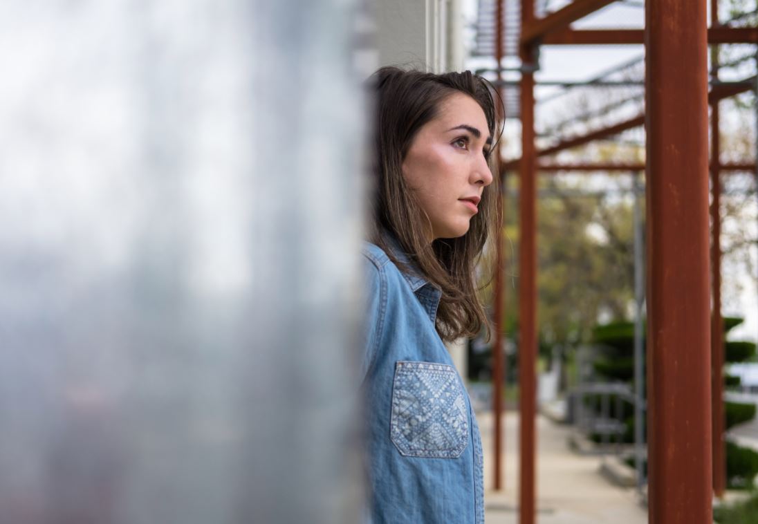 Woman in a blue blouse standing beside a pale pillar and looking outdoors.